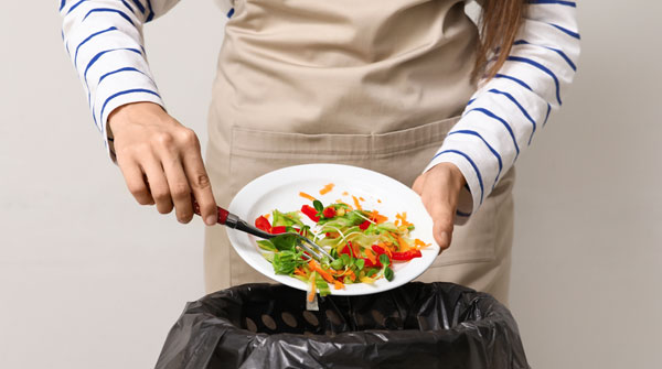 persona butta cibo dal piatto alla pattumiera